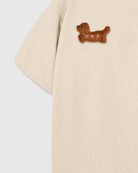 Detail of single plush dachshund on cream cotton sleeve showing brown fur and embroidered features