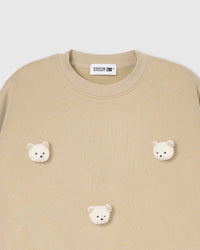 Close-up of plush teddy bear face with gingham-check ears on beige cotton showing tonal warmth