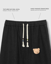 Close-up of elastic waistband with cream drawstring cords and plush teddy bear face on black wool drape pants with fabric callouts