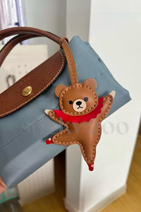 Both editions of the ballet bear charm — leather strap loop for bags, or 18K gold-plated keychain clip.