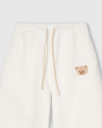 Close-up of check-ear plush teddy bear face on white cotton sweatpant showing gingham ear detail