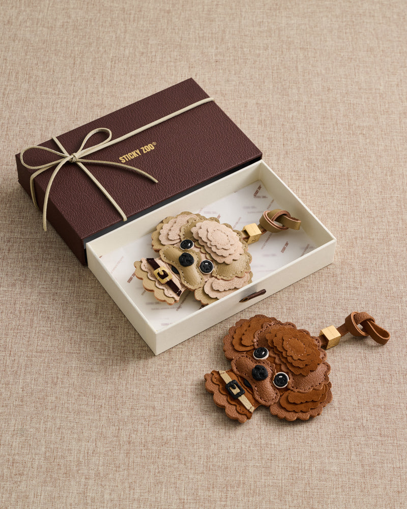 {{The gift they keep forever.}} Brown and cream poodle charms in ribbon-tied gift box — French Alran goatskin, alcantara suede, 72 hours of handcraft per piece.