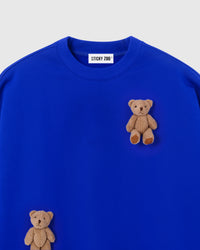 Close-up of dual plush teddy bear appliques on blue 450gsm cotton fleece showing 3D texture