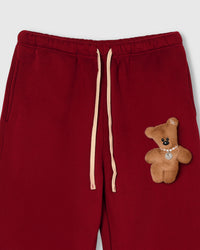Close-up of waistband area showing full-body plush teddy bear with pearl necklace on red cotton