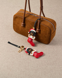 Handmade Santa Dachshund Stocking leather bag charm clipped to a cream canvas handbag — French Alran goatskin holiday charm, 7-day artisan build. STICKYZOO.