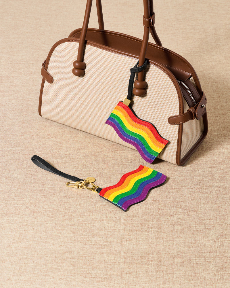 Both pride flag charm attachments with cream and black bags on beige linen surface by STICKYZOO