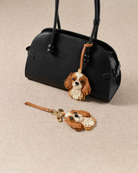 Both Cavalier King Charles editions styled with bag — strap loop and keychain clip. French Alran goatskin, alcantara suede, 18K gold-plated hardware.