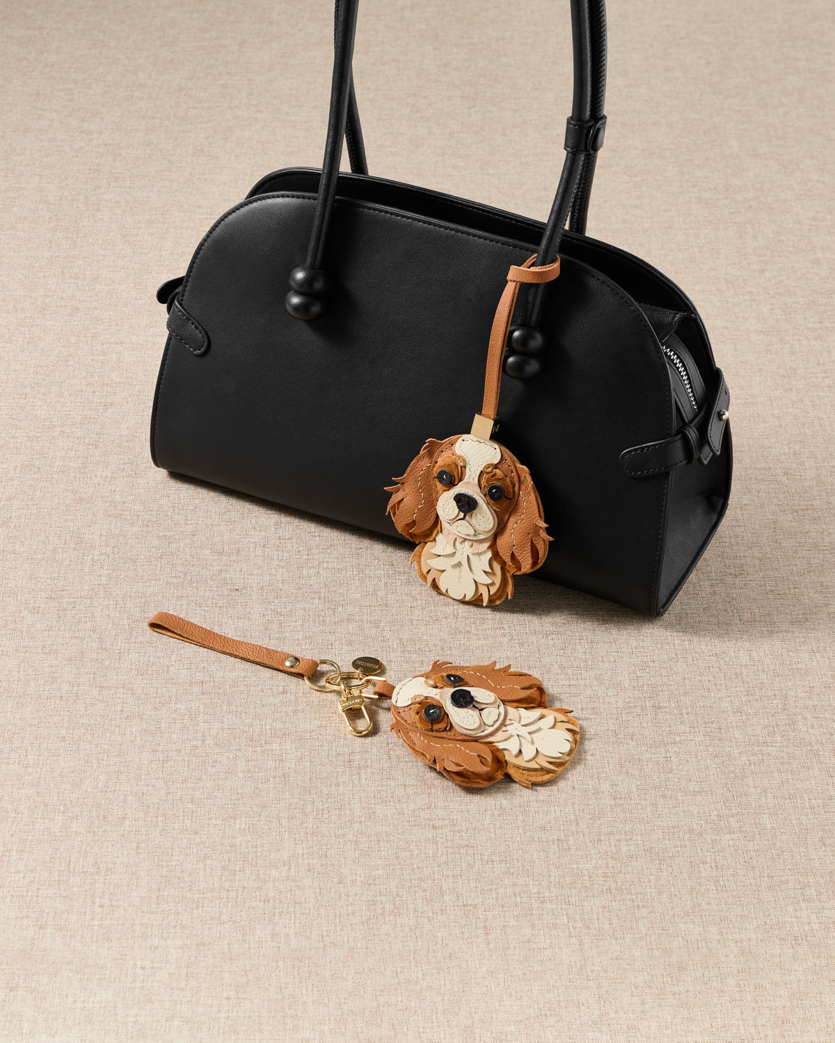 {{"People stop me to ask about it."}} Both Cavalier King Charles editions styled with bag — strap loop and keychain clip. French Alran goatskin, alcantara suede, 18K gold-plated hardware.