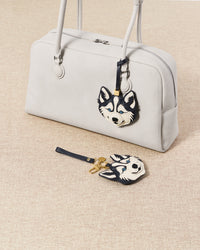 Two husky charms with grey bag and blue bag flat-lay on beige linen surface