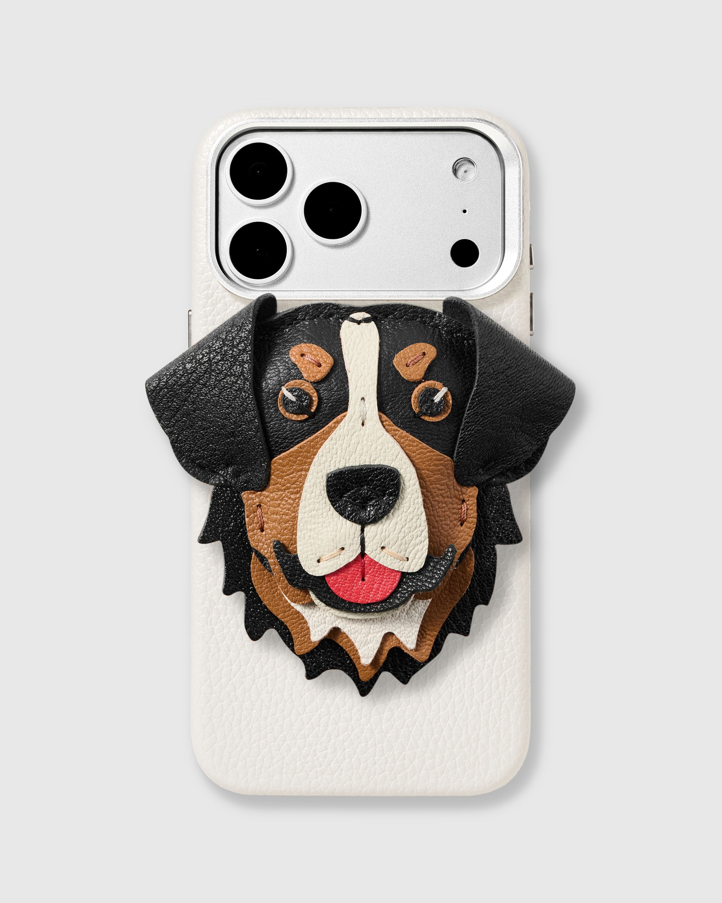 Mountain Charm Case with handmade French Alran leather Bernese Mountain Dog charm — hand-cut ears, stitched eyebrows, layered tri-color coat on white textured leather case. Rated 4.9 stars.
