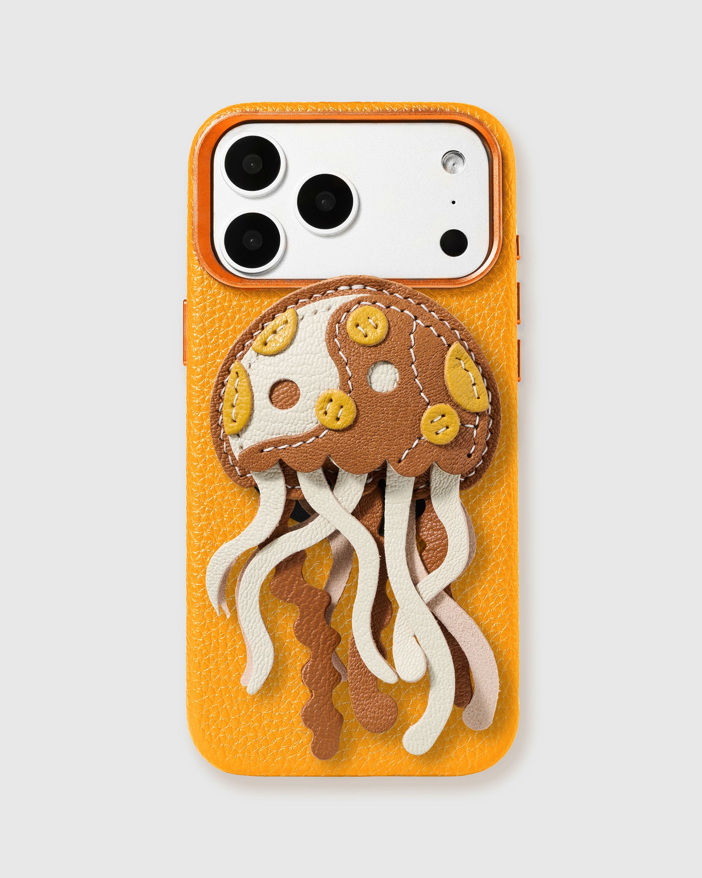 STICKYZOO Spotted Jellyfish Charm Case in amber-orange with 3D handmade French Alran leather jellyfish charm featuring spotted bell and flowing leather tentacles in brown, cream, and blush tones.