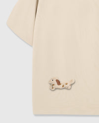 Detail of hand-stitched spotted dachshund on lower body area of beige tee showing long body shape