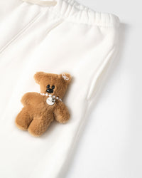 Close-up of full-body plush teddy bear on white cotton showing pearl necklace, pendant, and fur texture