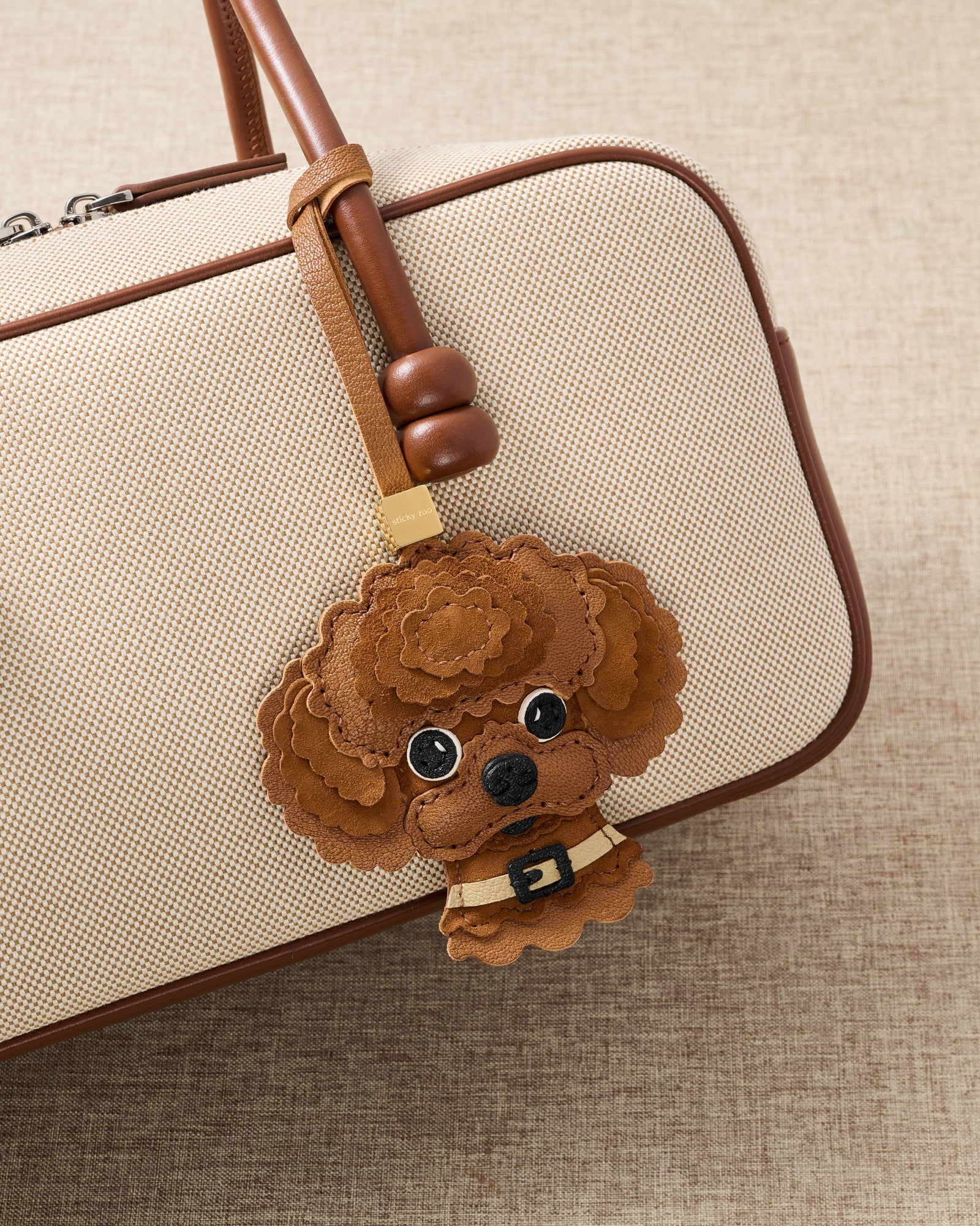 {{5,000+ Reviews.}} The Poodle Charm — 5,000+ reviews across STICKYZOO. French Alran × Alcantara, 7 days of hand-work per piece.