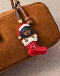 Handmade Santa Dachshund Stocking bag charm shown on a tan suede handbag — red leather stocking with embroidered snowflakes, dachshund in Santa hat. STICKYZOO holiday collectible.
