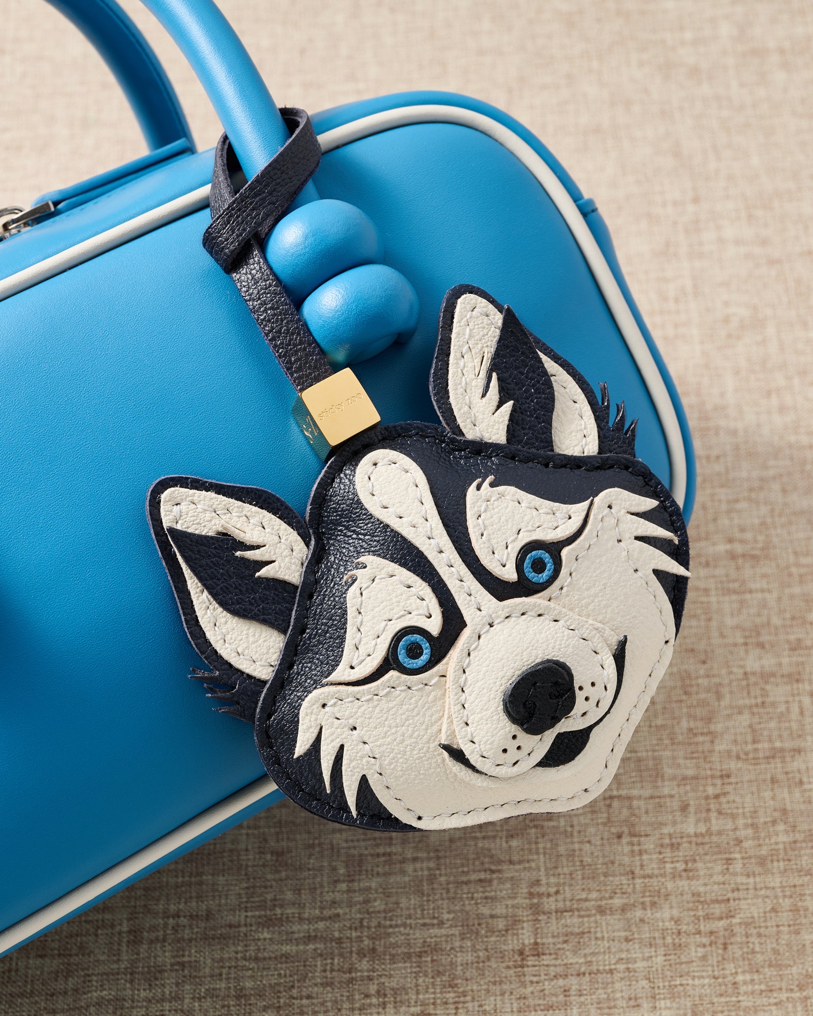 {{Every layer by hand}} Macro of husky charm on blue bag handle showing hand-stitched leather layers and ice-blue embroidered eyes