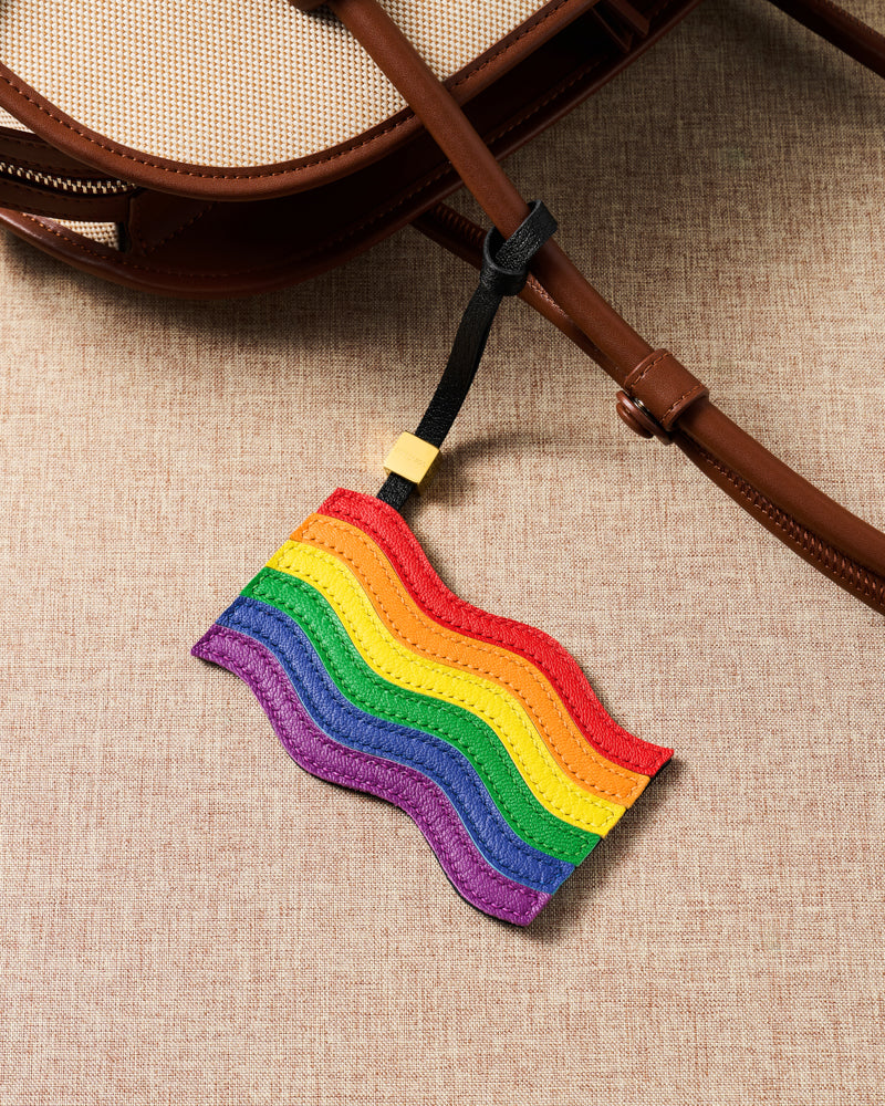 Close-up of handmade pride flag charm on canvas bag handle showing leather grain and stitching