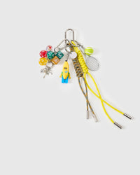 Handmade stack charm | STICKYZOO Banana Rally Stack Charm flat lay featuring banana-costumed collectible figure, colorful gaming dice, mini tennis racket and felt tennis ball, heart padlock with keys, and yellow and multicolor hand-braided paracord ropes with stainless steel tips