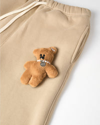 Close-up of plush teddy bear with pearl necklace on cream cotton sweatpant showing 3D texture