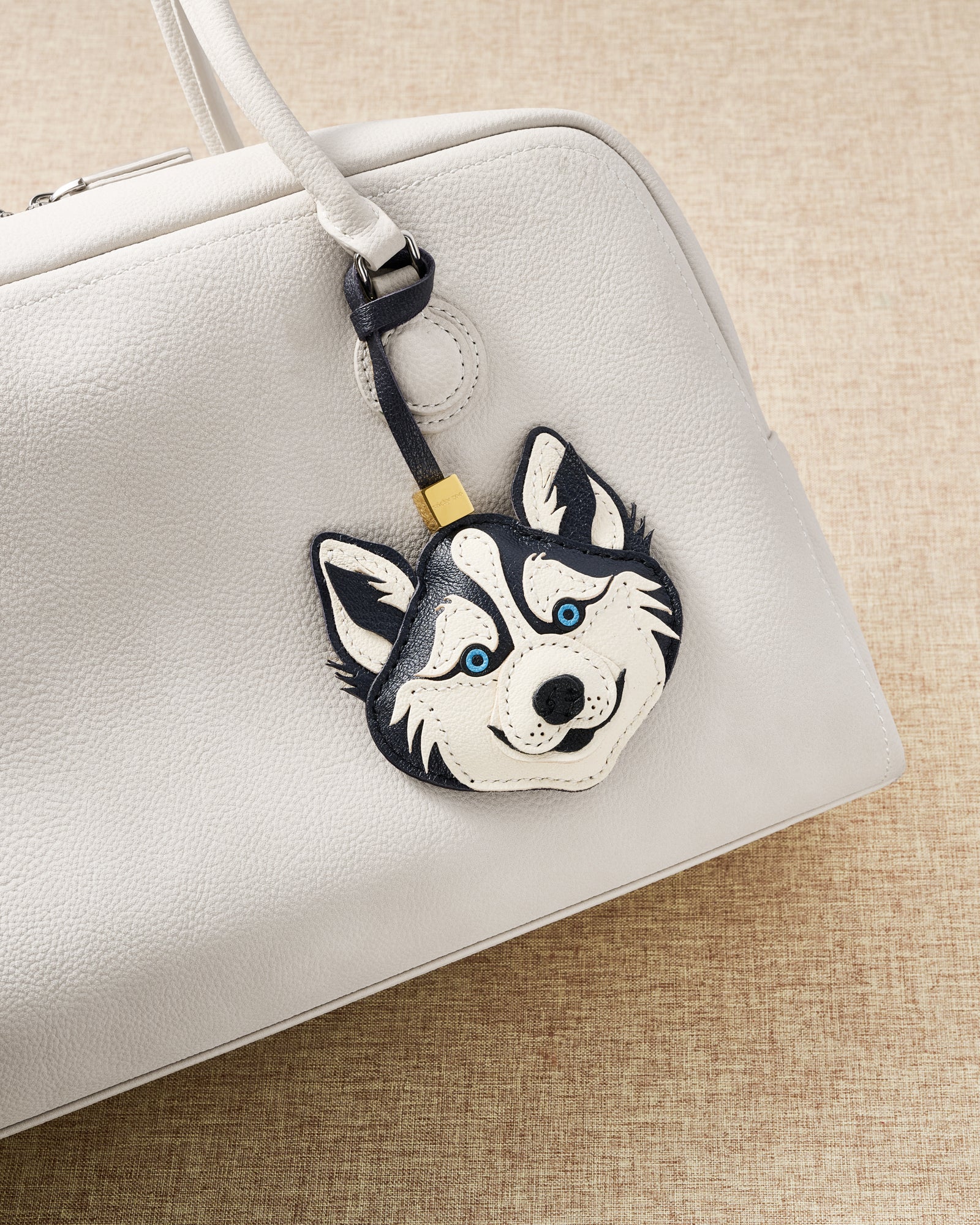 {{5,000+ verified reviews}} STICKYZOO husky charm draped on cream leather bag in warm natural light