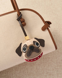 The Pug Charm — real full-grain leather from Tarn, France. Red studded collar. Four days by hand. Arrives in luxury gift packaging.