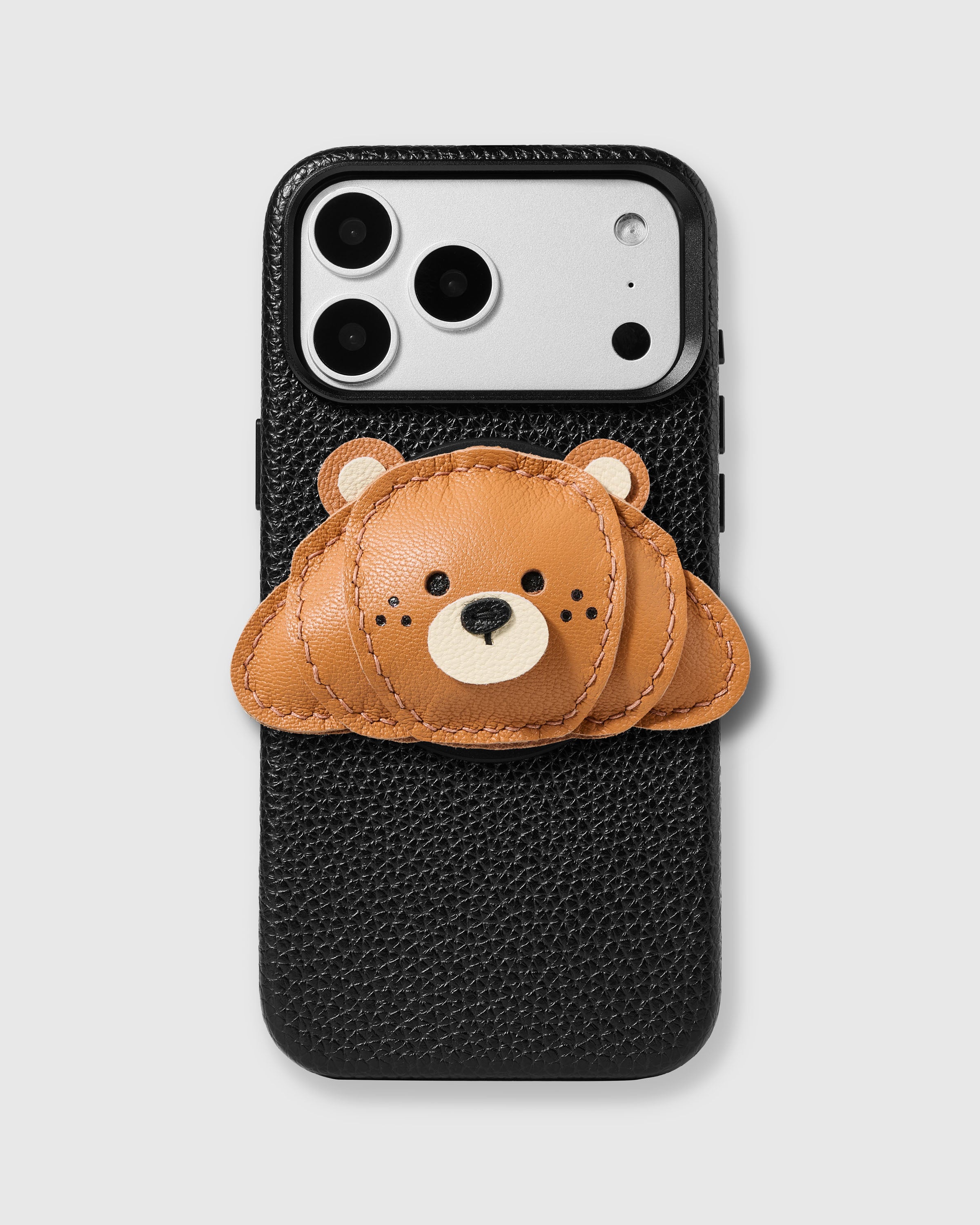 STICKYZOO Croissant Charm Case in black with 3D handmade French Alran leather croissant charm in golden-brown tones with layered ridges and hand-stitched detail.