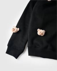 Close-up of plush bear faces on sleeve and lower hem area showing ribbed cuffs on black cotton
