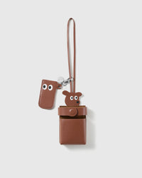 STICKYZOO tan leather cigarette case in French Alran goatskin, with a brown bear head peeking over the top rim, a press-stud flap, a separate eyes tab on the clasp, an engraved silver STICKYZOO disc, and a long leather carry strap for a bag.