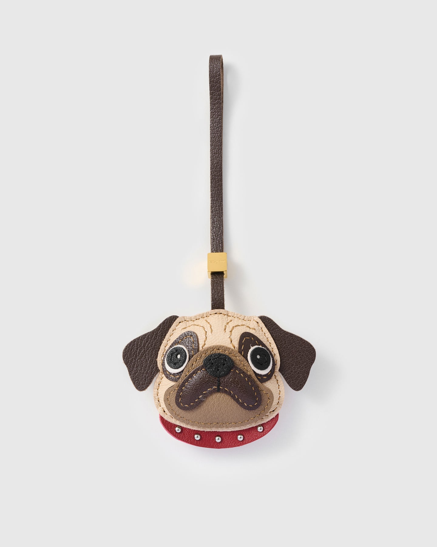{{French leather. 4 days.}} The Pug Charm — exclusive drop from STICKYZOO. Hand-cut French Alran goatskin, cream-beige face with hand-stitched wrinkle lines, dark brown muzzle, sparkly black nose, red studded collar, dark brown leather strap. Four days per piece. Designed in Amsterdam.