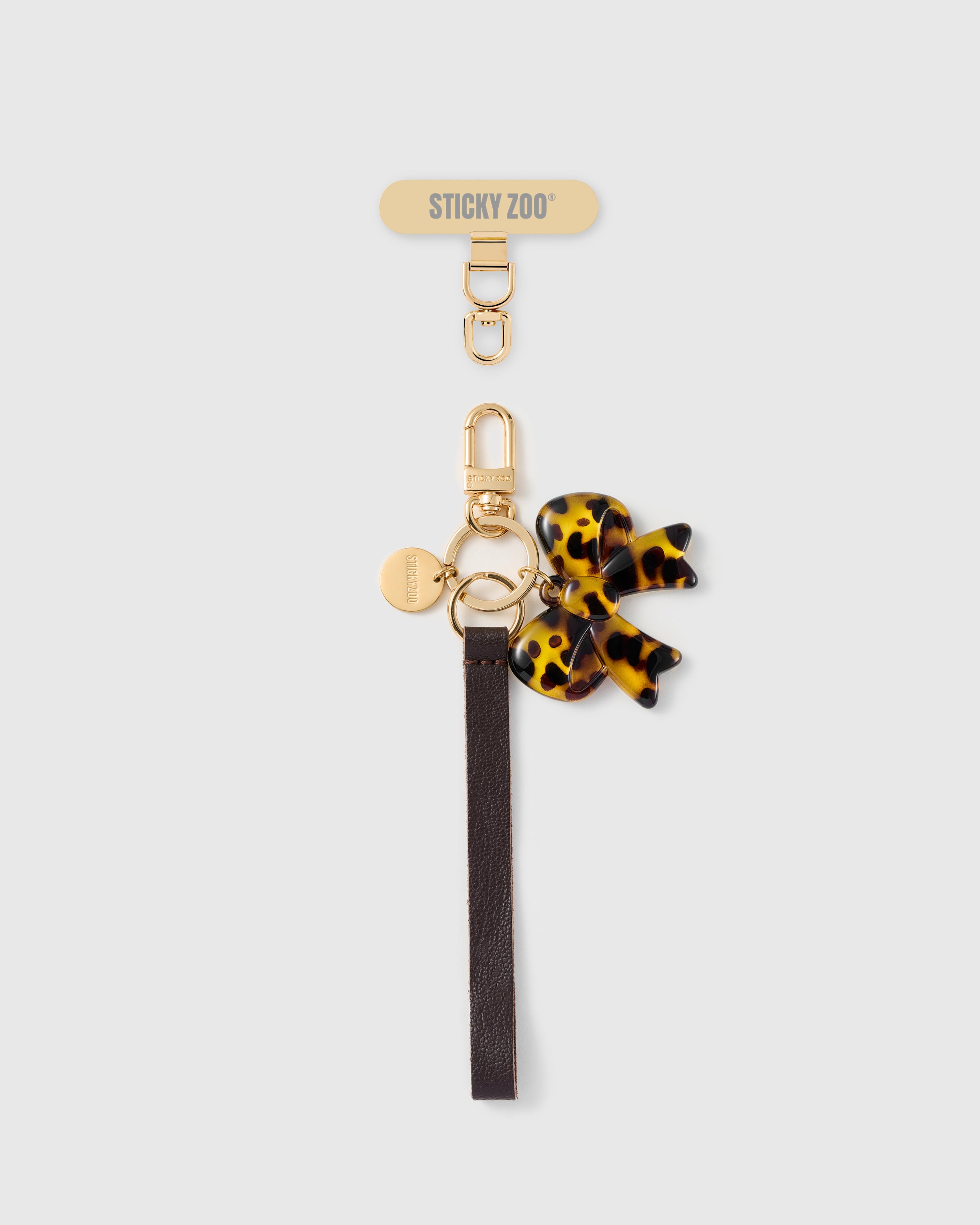 Handmade French Alran cocoa brown leather phone strap with tortoise-shell acetate bow charm and 18K gold STICKYZOO hardware