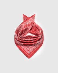 Red bandana silk scarf coiled on a white surface showing the ivory line-work and silk drape