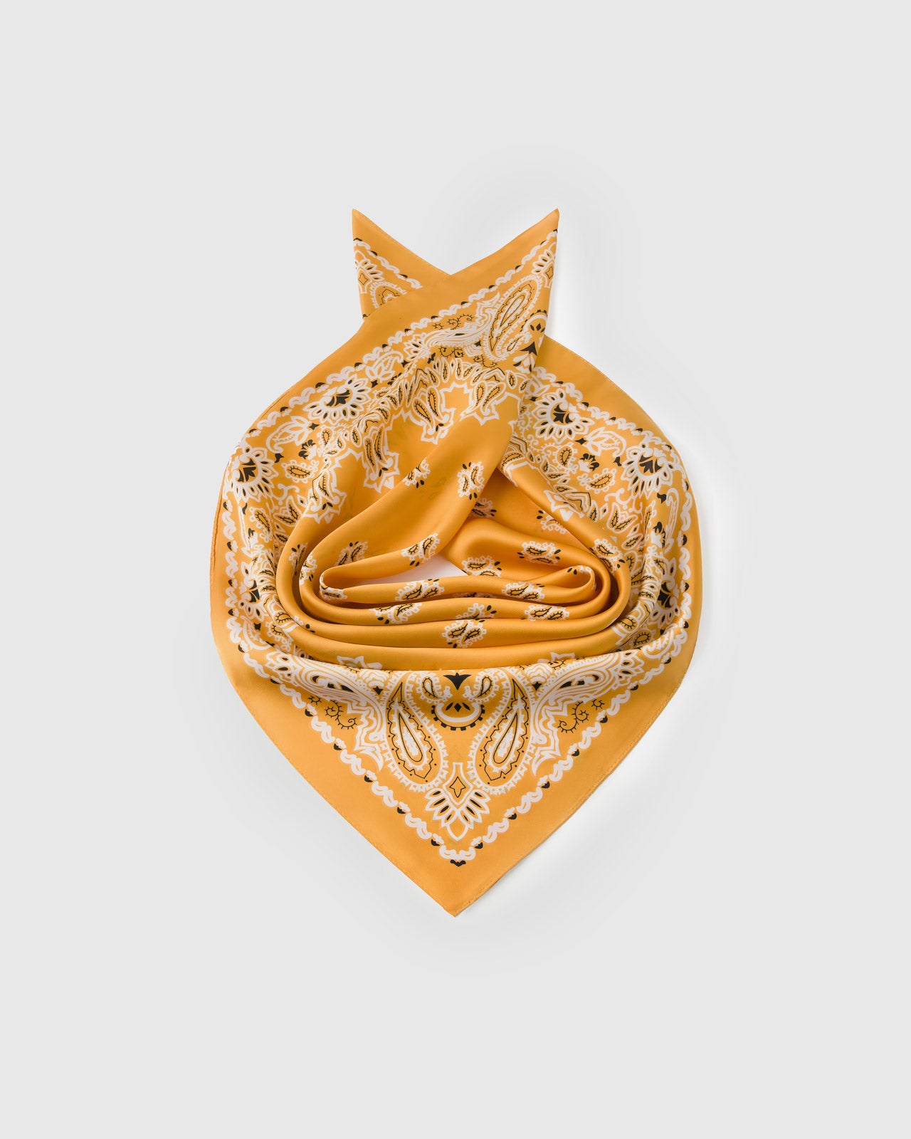 Saffron silk paisley scarf coiled to show the soft drape and the bandana motif catching the light