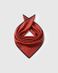 Silk equestrian scarf coiled to show the pure silk drape and the stirrup repeat on saddle red