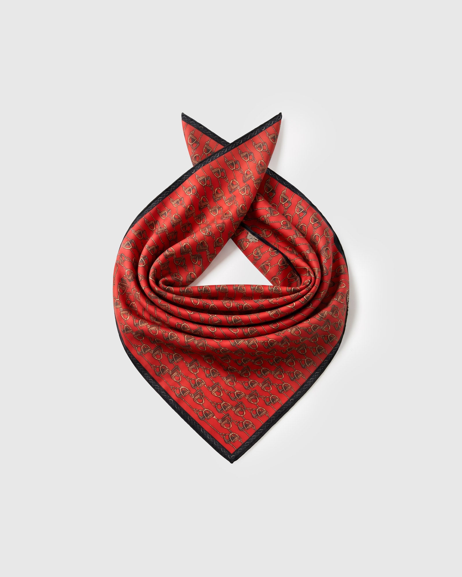 Silk equestrian scarf coiled to show the pure silk drape and the stirrup repeat on saddle red