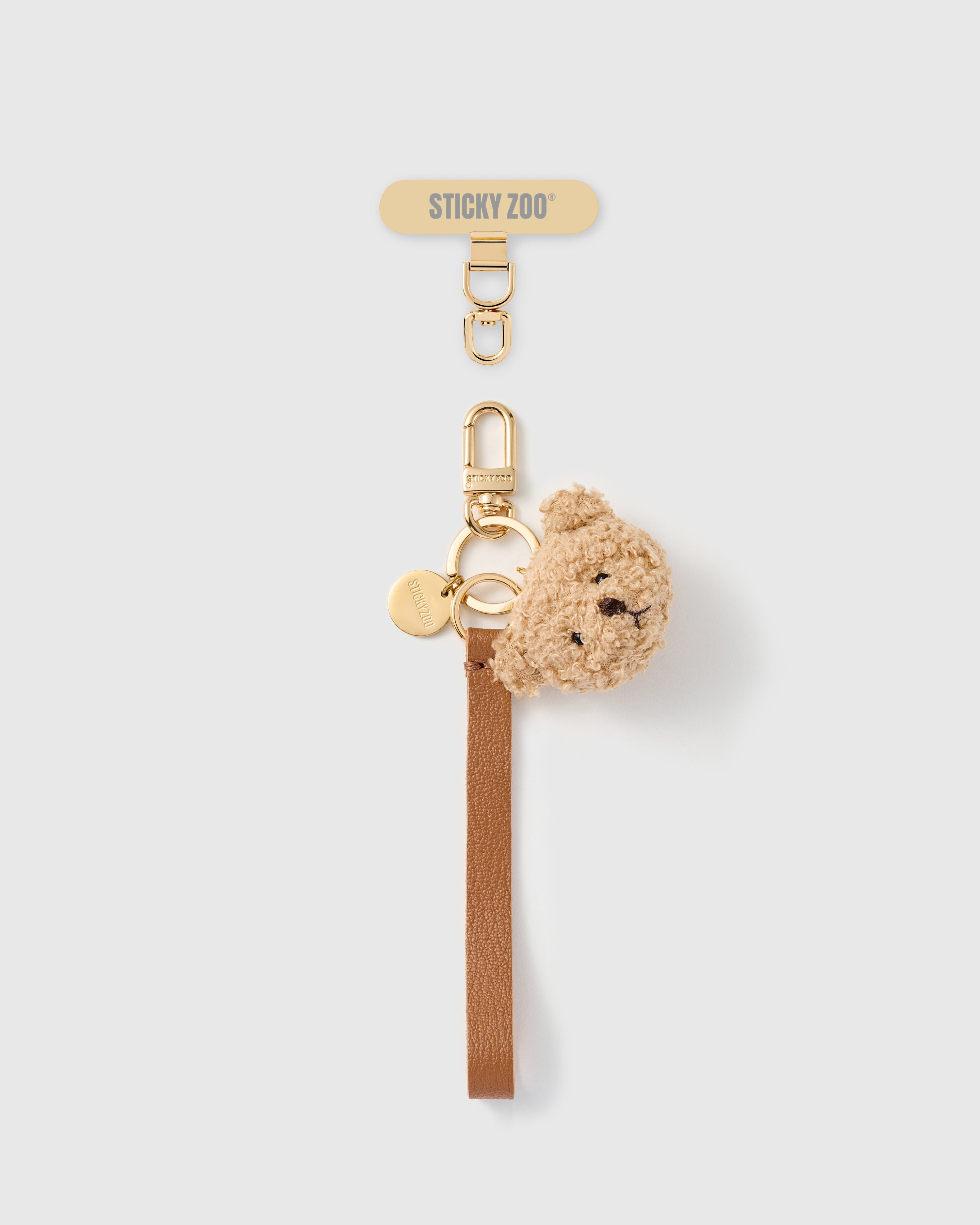 Handmade French Alran cocoa tan leather phone strap with small plush bear-head charm and 18K gold STICKYZOO hardware