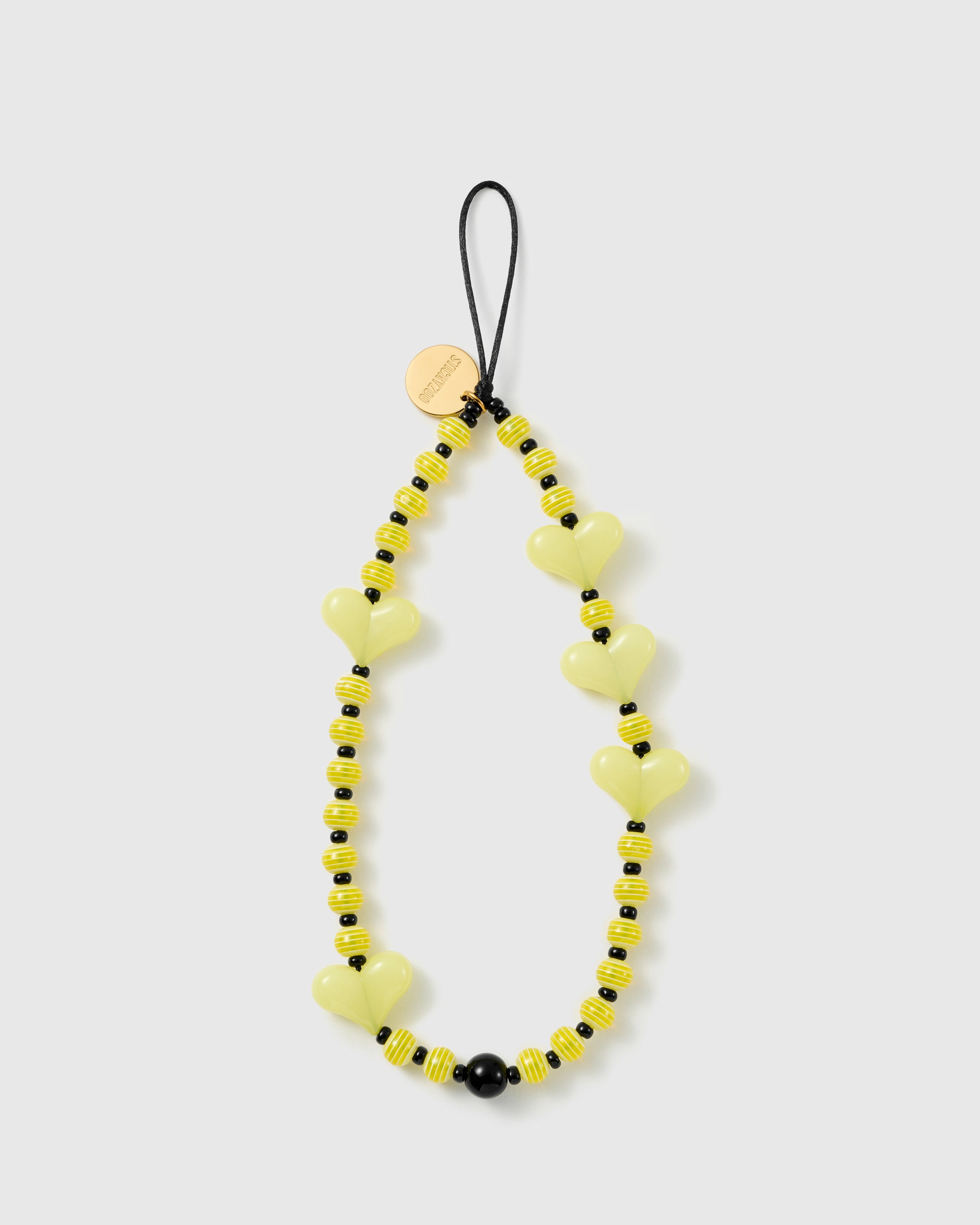 STICKYZOO Lemon Heart phone strap flat: pale yellow glossy heart beads, yellow-and-white striped beads and black spacers on a black cord loop with gold disc