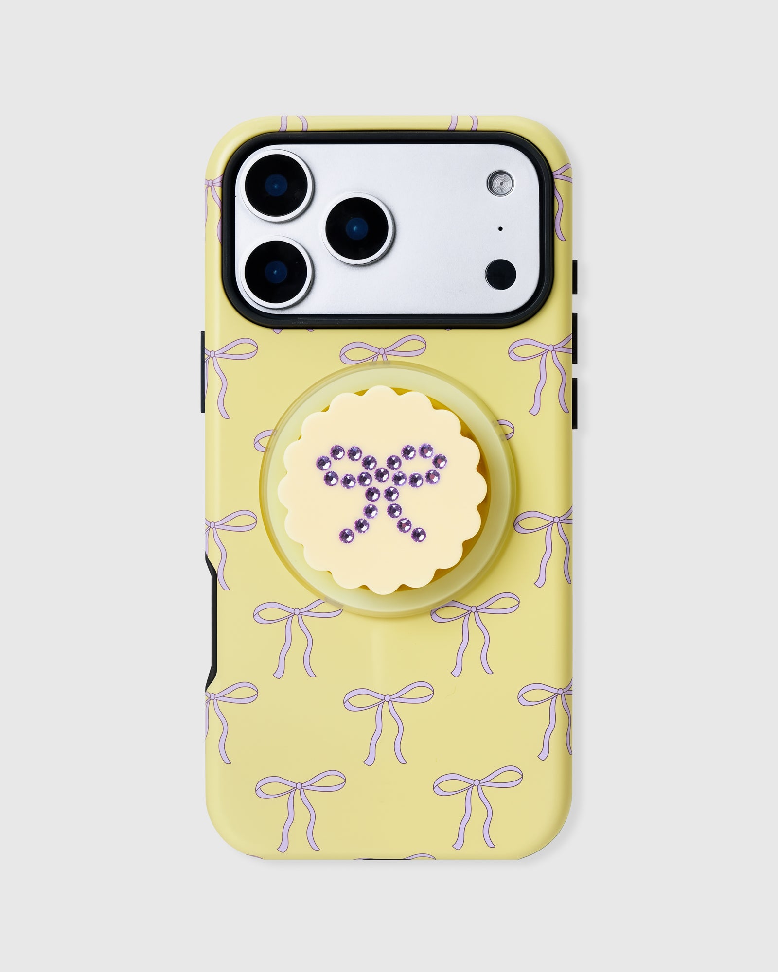 Butter-yellow STICKYZOO phone case with a lilac bow print and a built-in MagSafe grip topped by a rhinestone bow medallion