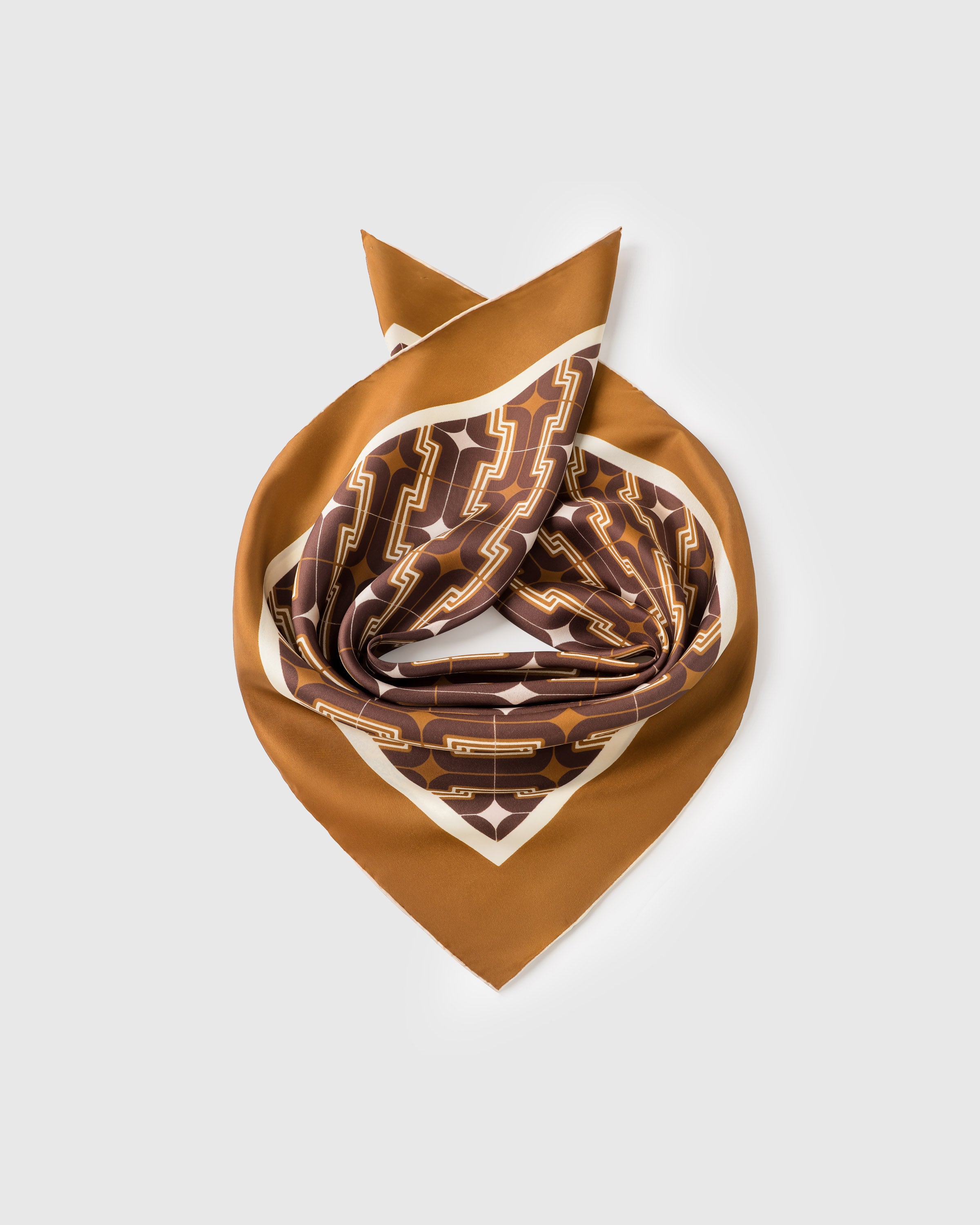 Silk deco scarf coiled to show the soft drape of pure silk and the cognac geometric print