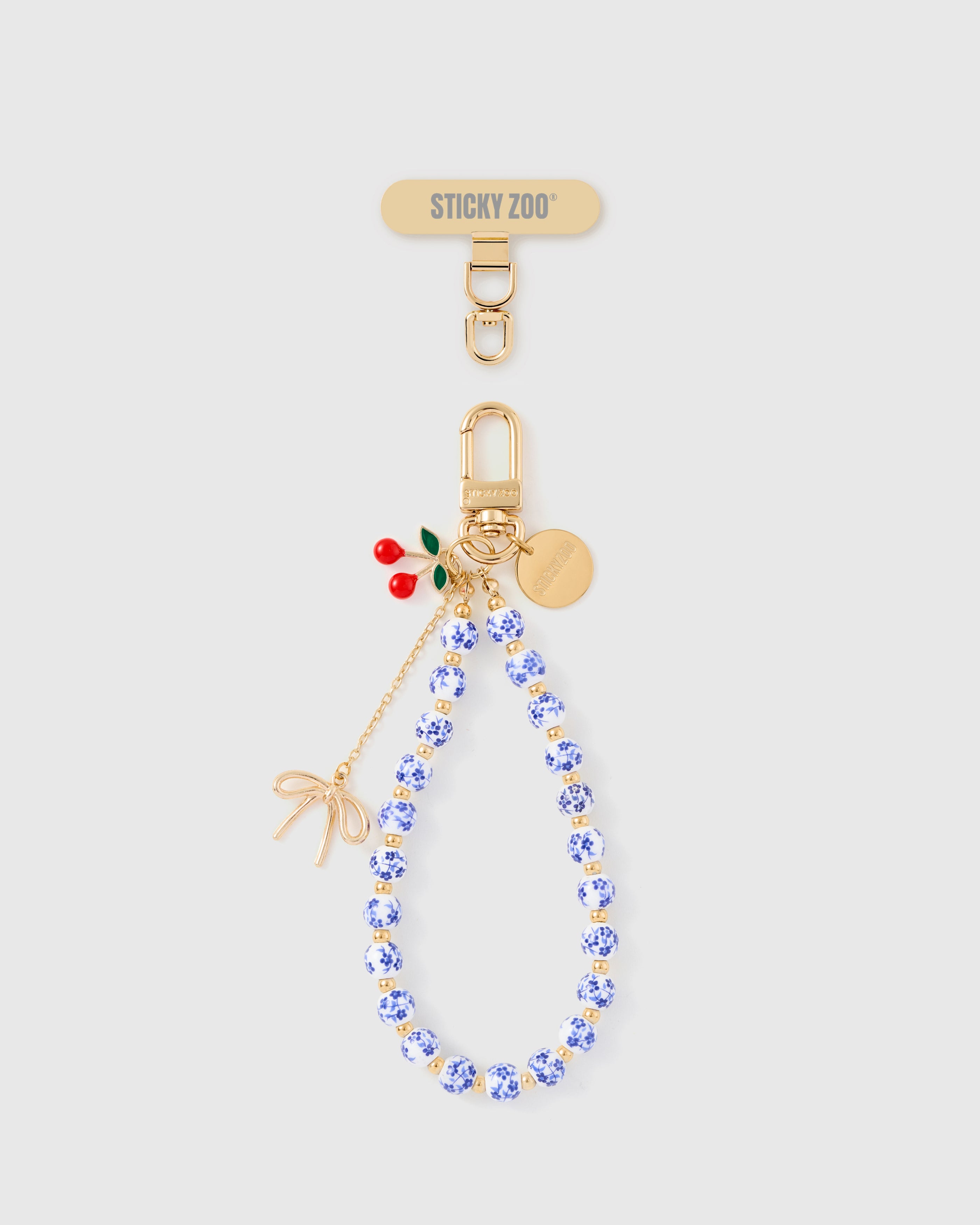 Handmade blue-and-white porcelain phone strap with red cherry charm and gold bow by STICKYZOO