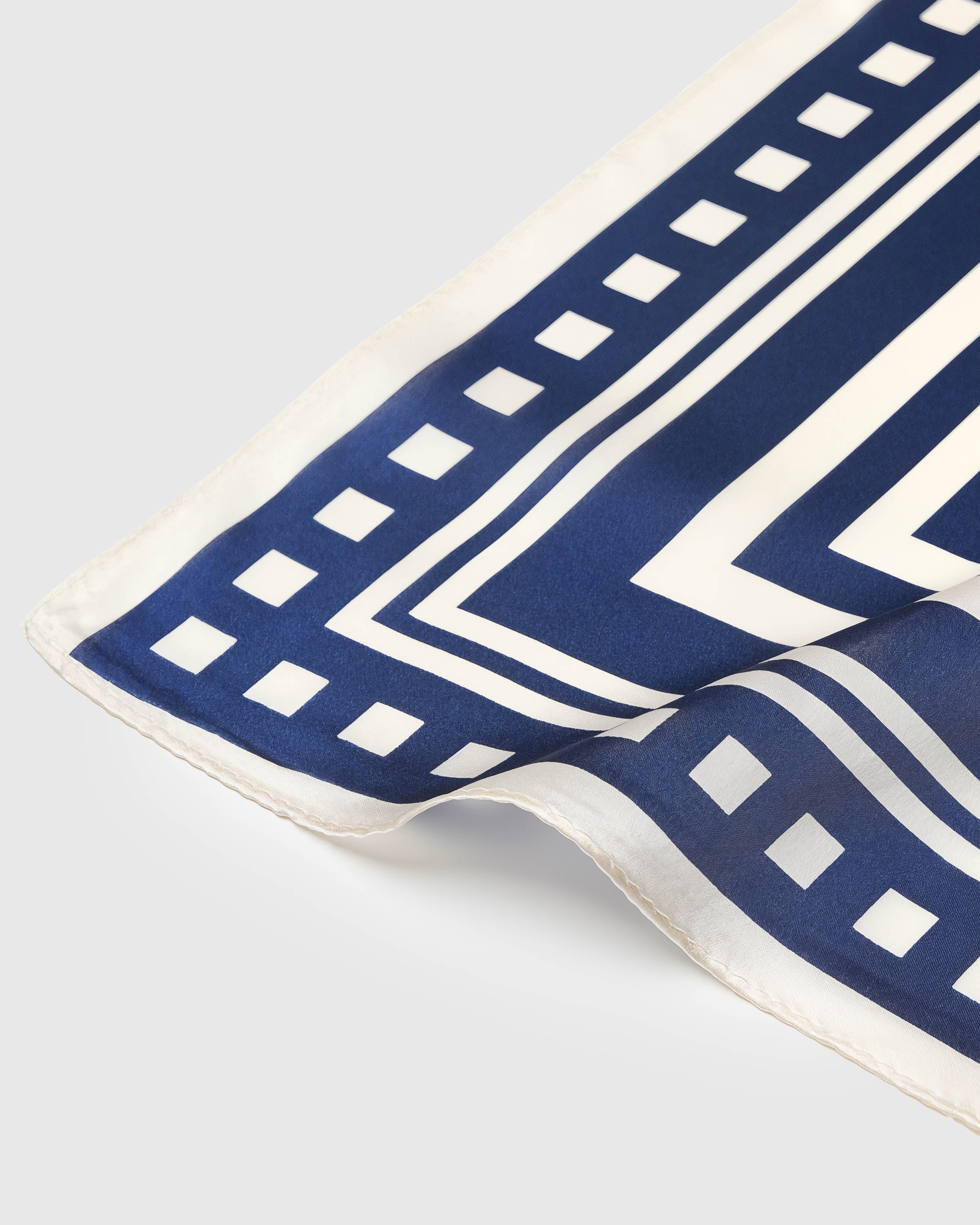 Close-up of the ivory checker-bar border meeting the navy chevron field on pure silk