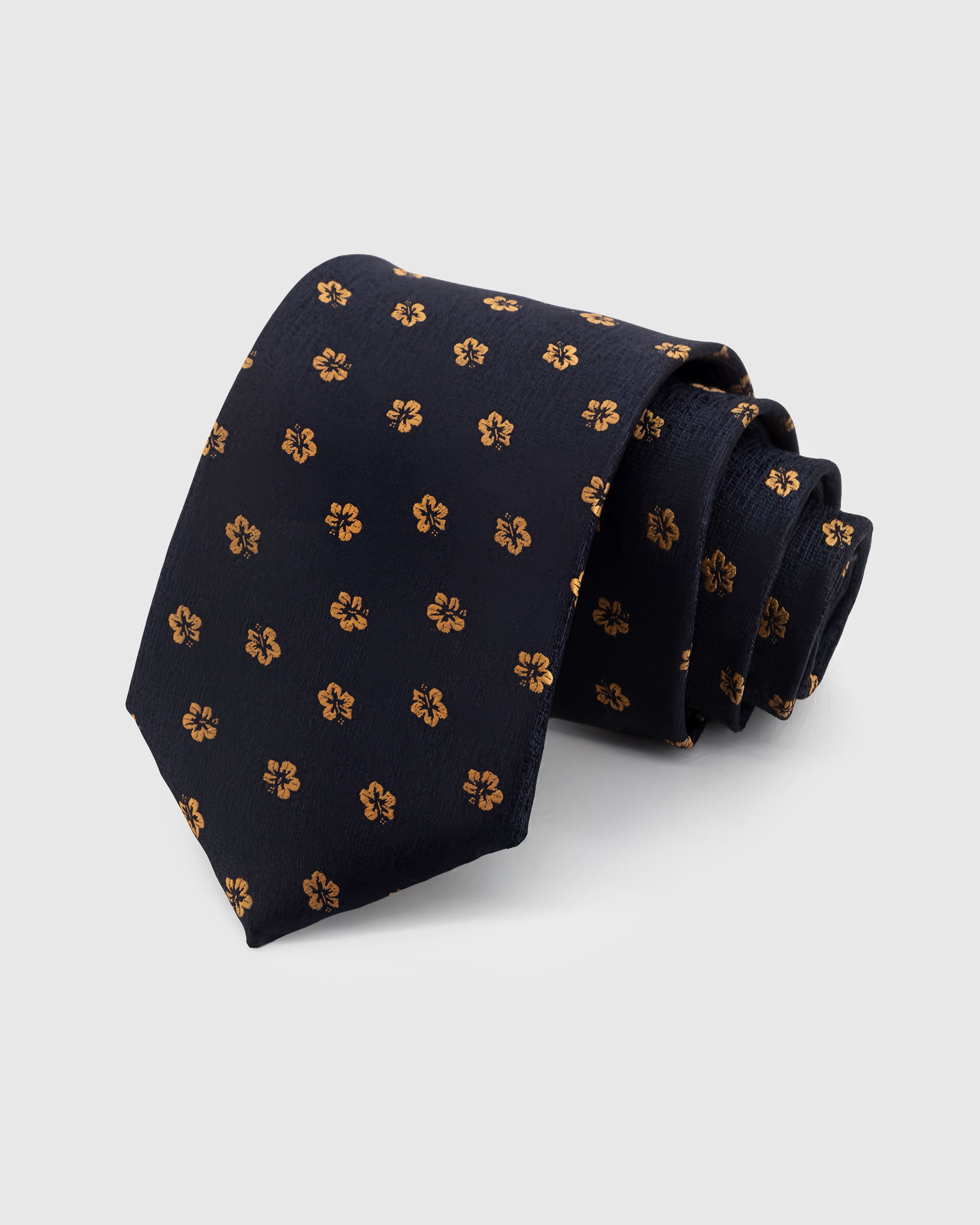 STICKYZOO NAVY HIBISCUS TIE — 100% mulberry silk with hand-embroidered golden amber hibiscus bloom motifs on deep navy with slubbed texture ground