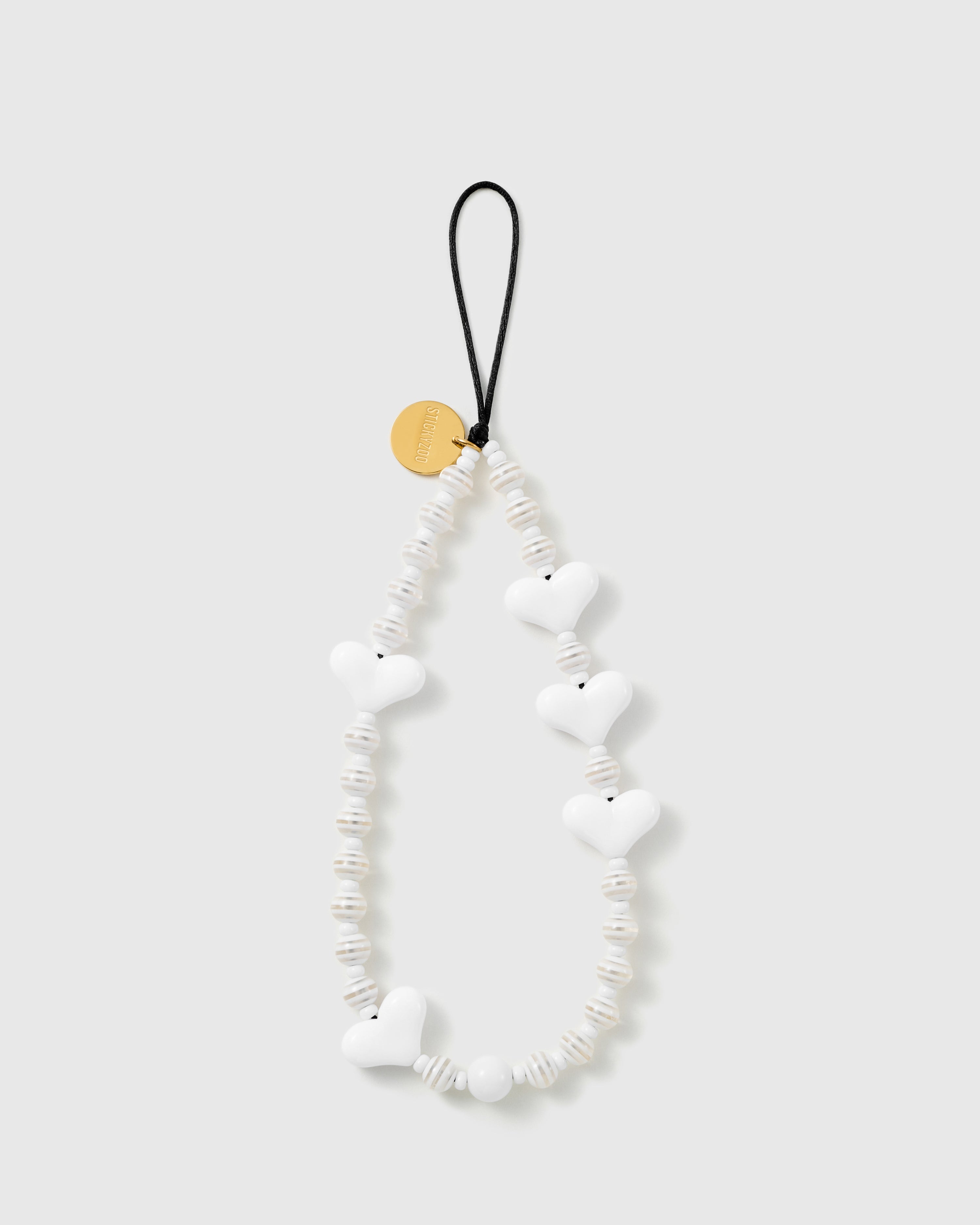 STICKYZOO Snow Heart phone strap laid flat, glossy white puffy heart beads and ribbed cream-white disc beads on a black stretch-cord loop with a gold-tone disc.
