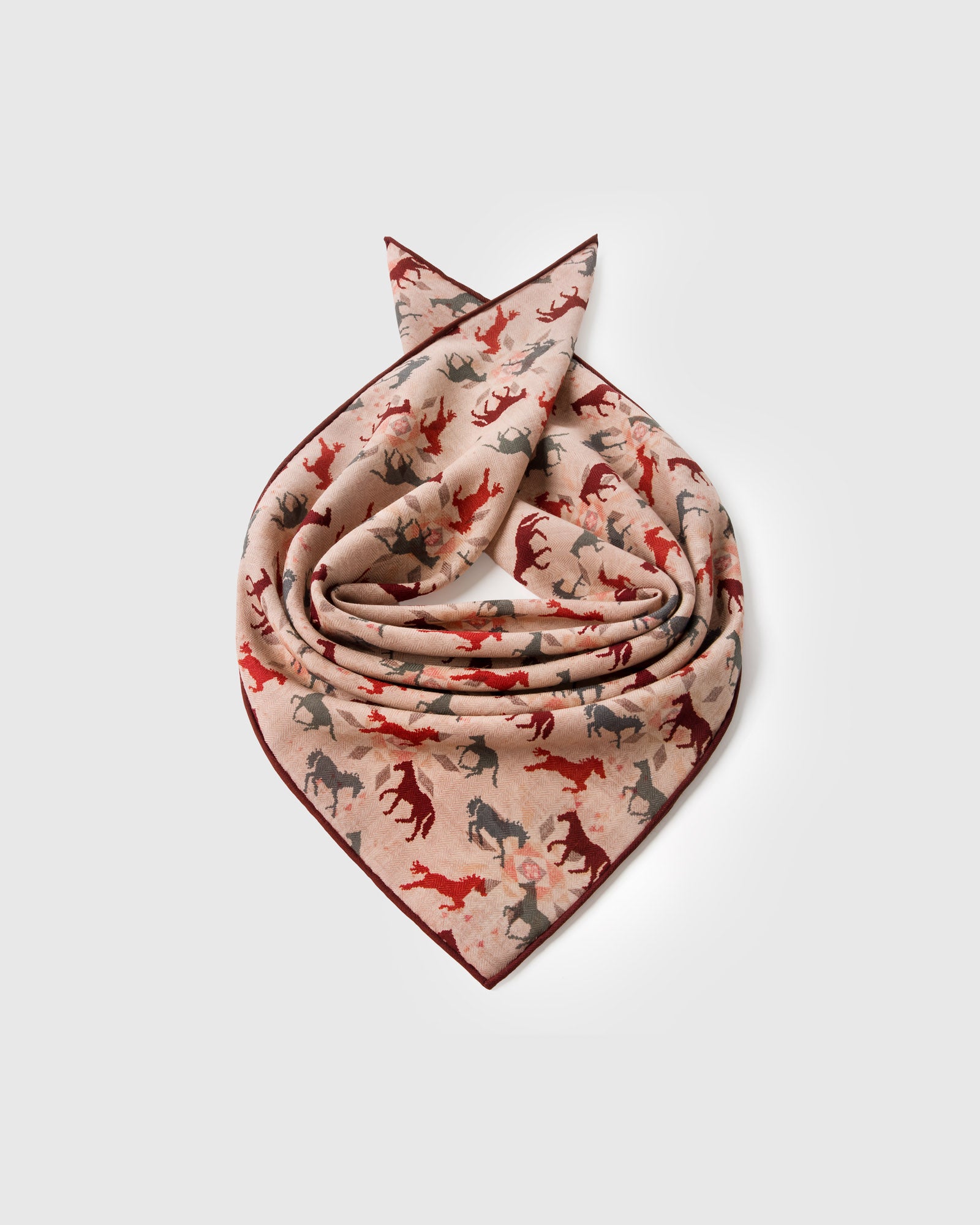 Silk horse-print scarf coiled to show the soft drape and the burgundy border catching light