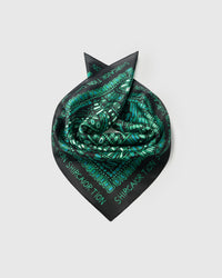 Silk scarf coiled into a rosette showing the soft drape and the emerald dotwork holding saturated color