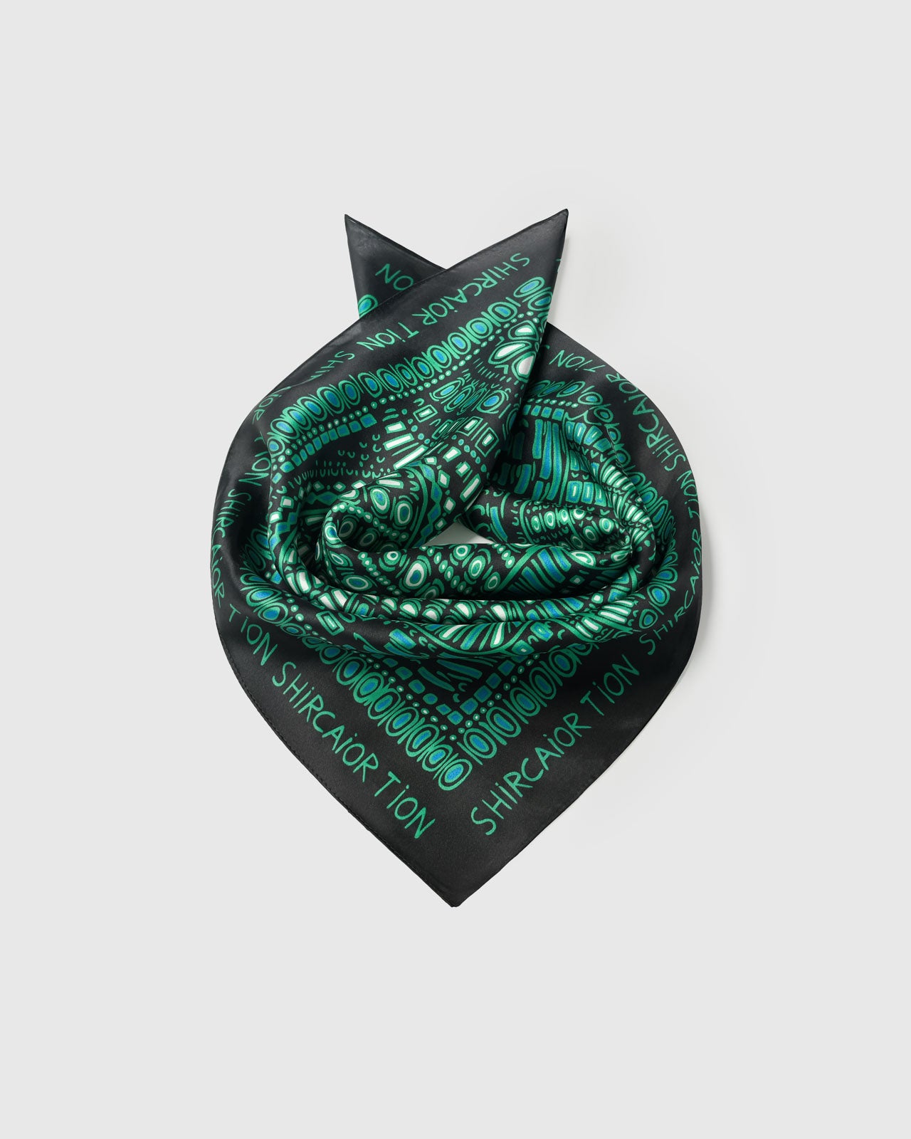 Silk scarf coiled into a rosette showing the soft drape and the emerald dotwork holding saturated color