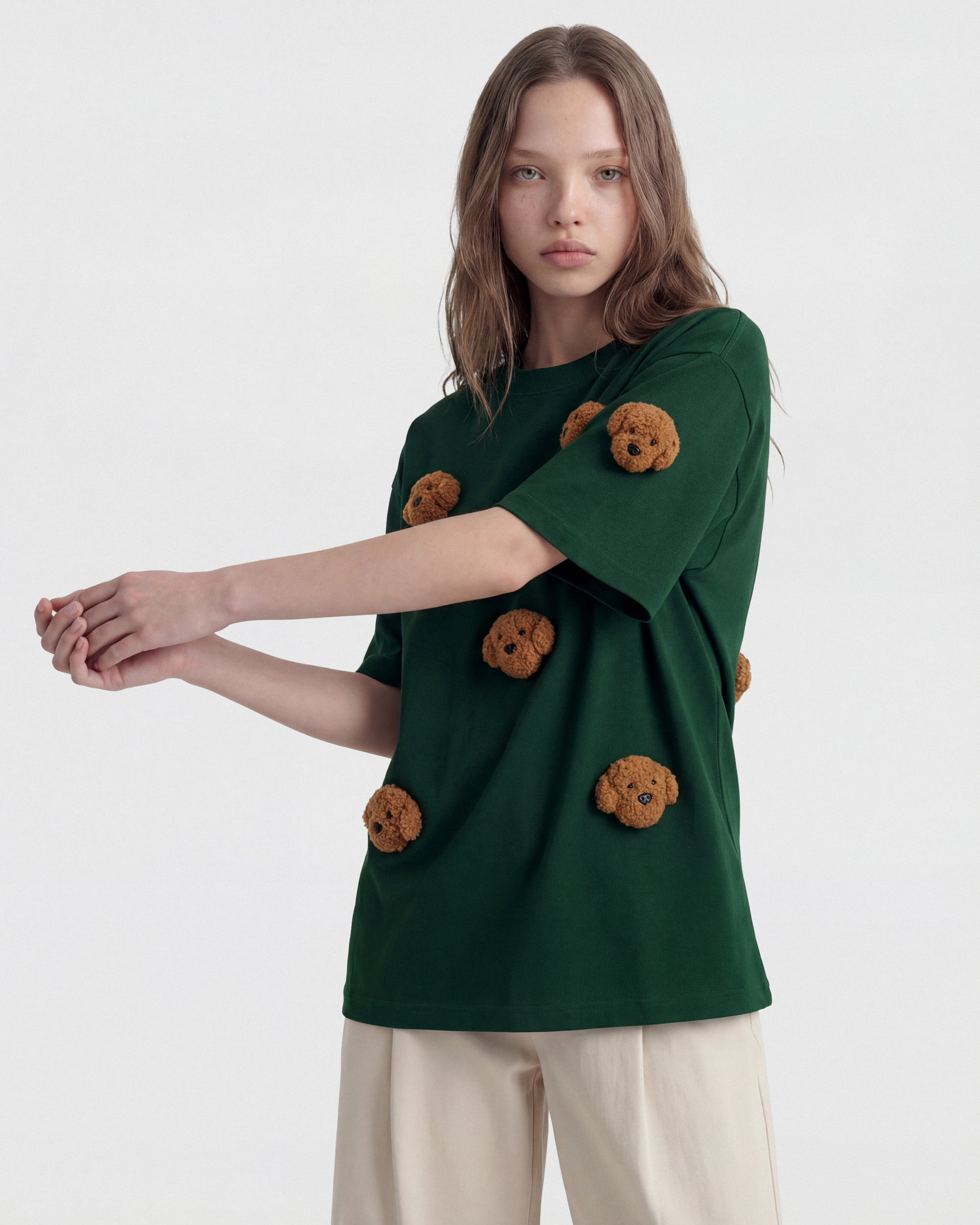 {{Not printed — stitched}} Model in green Poodle Parade T-Shirt angled pose showing plush poodle appliques