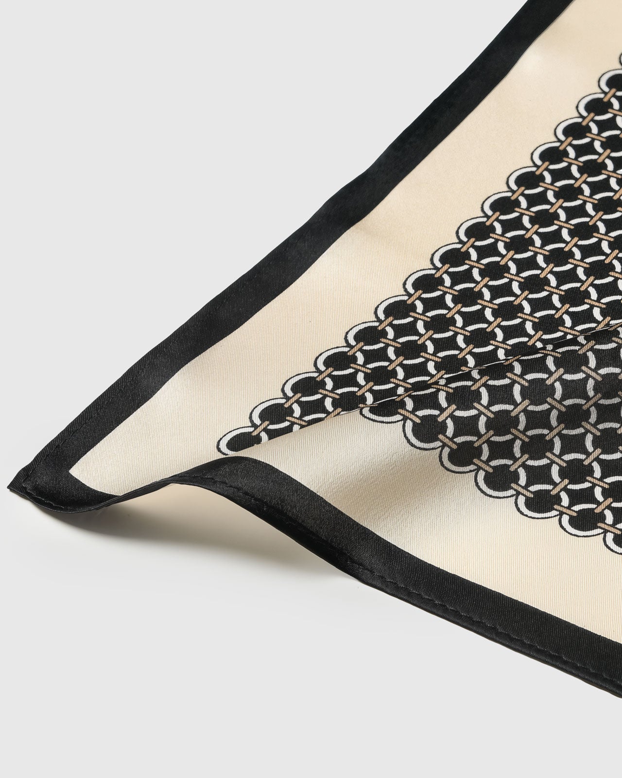 Silk chain link scarf coiled through a leather ring showing the ivory grid on black