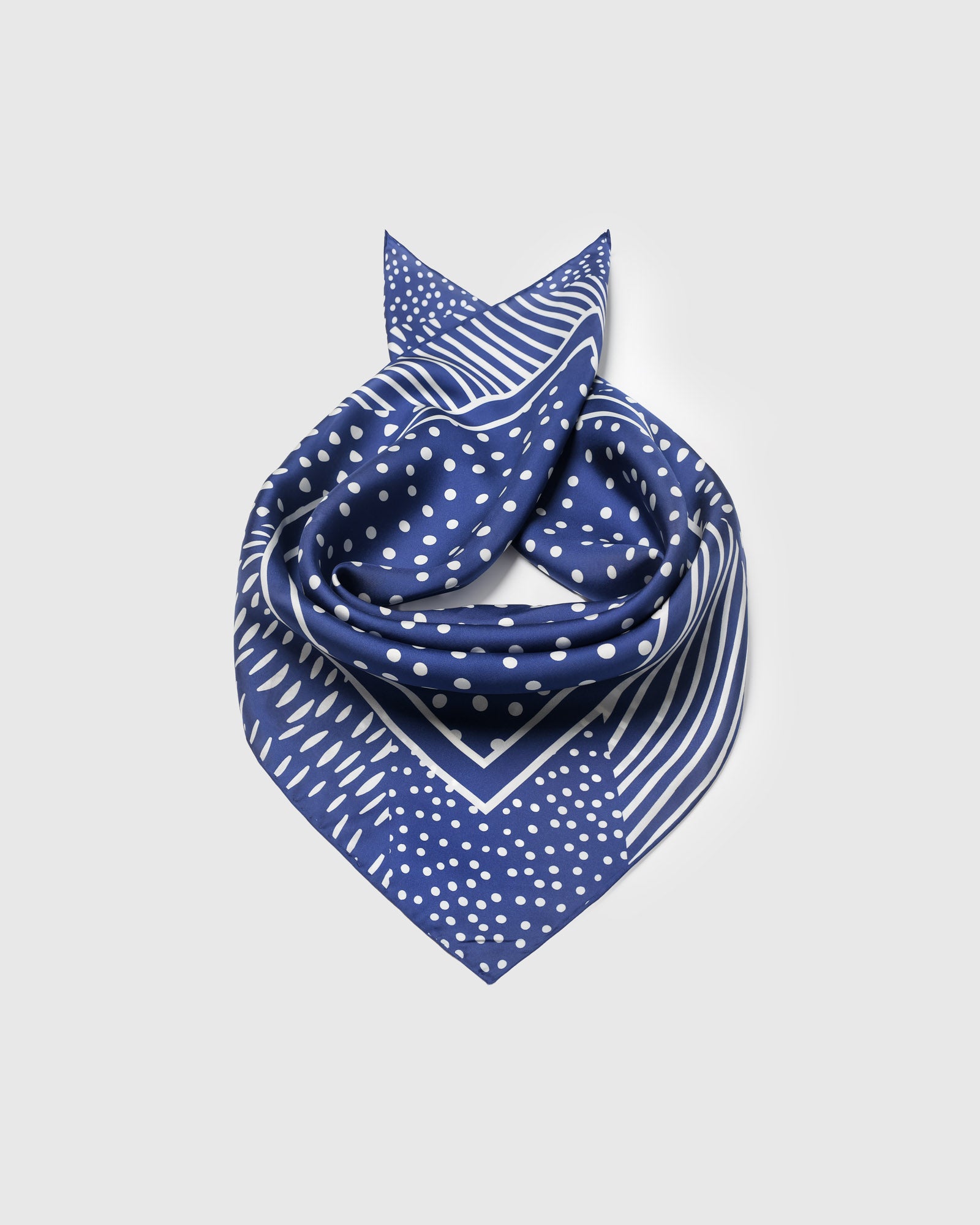 Cobalt silk scarf coiled to show the small-dot center field framed by an ivory line border