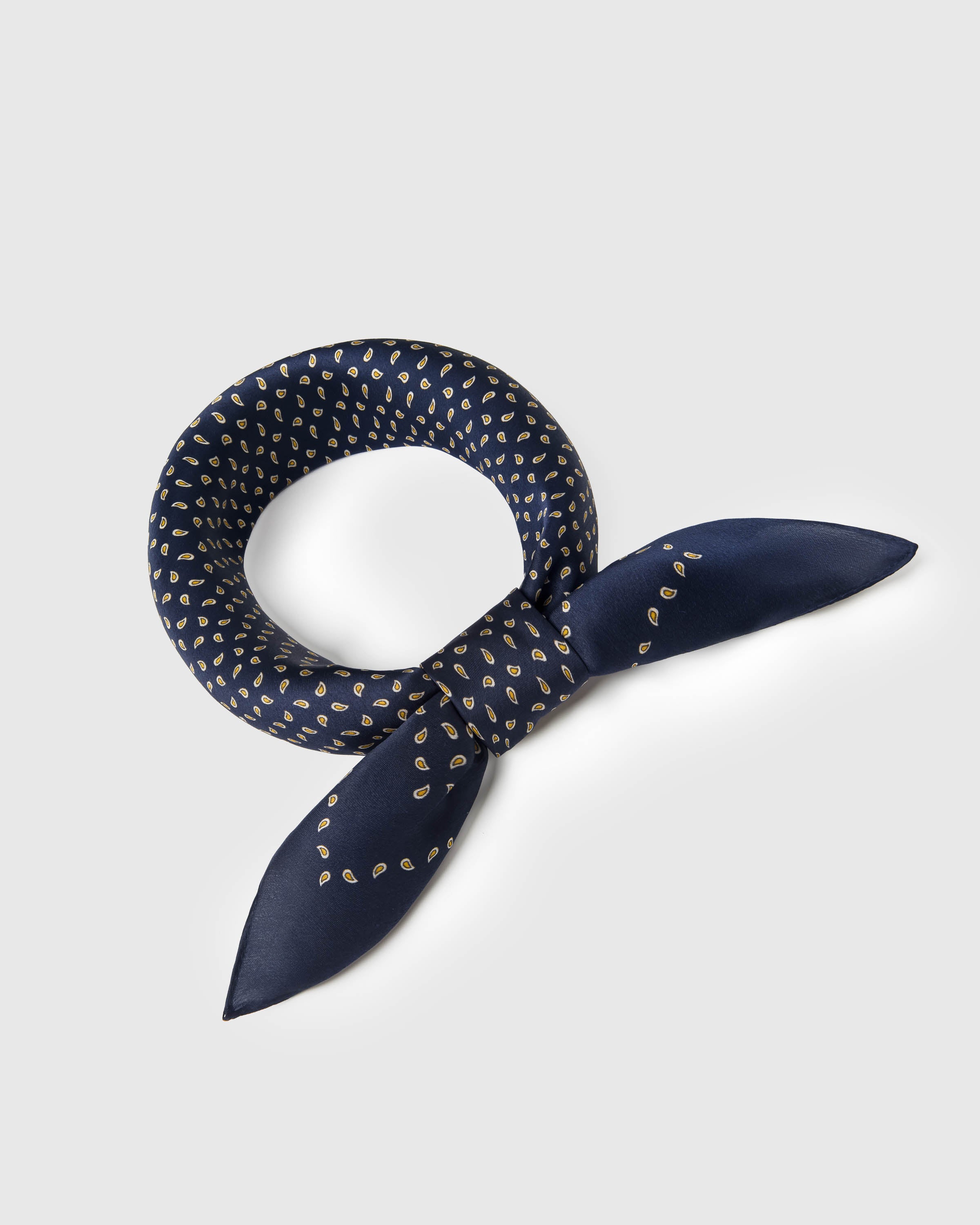 Navy silk paisley scarf knotted into a ring showing the soft drape and the gold seed motif