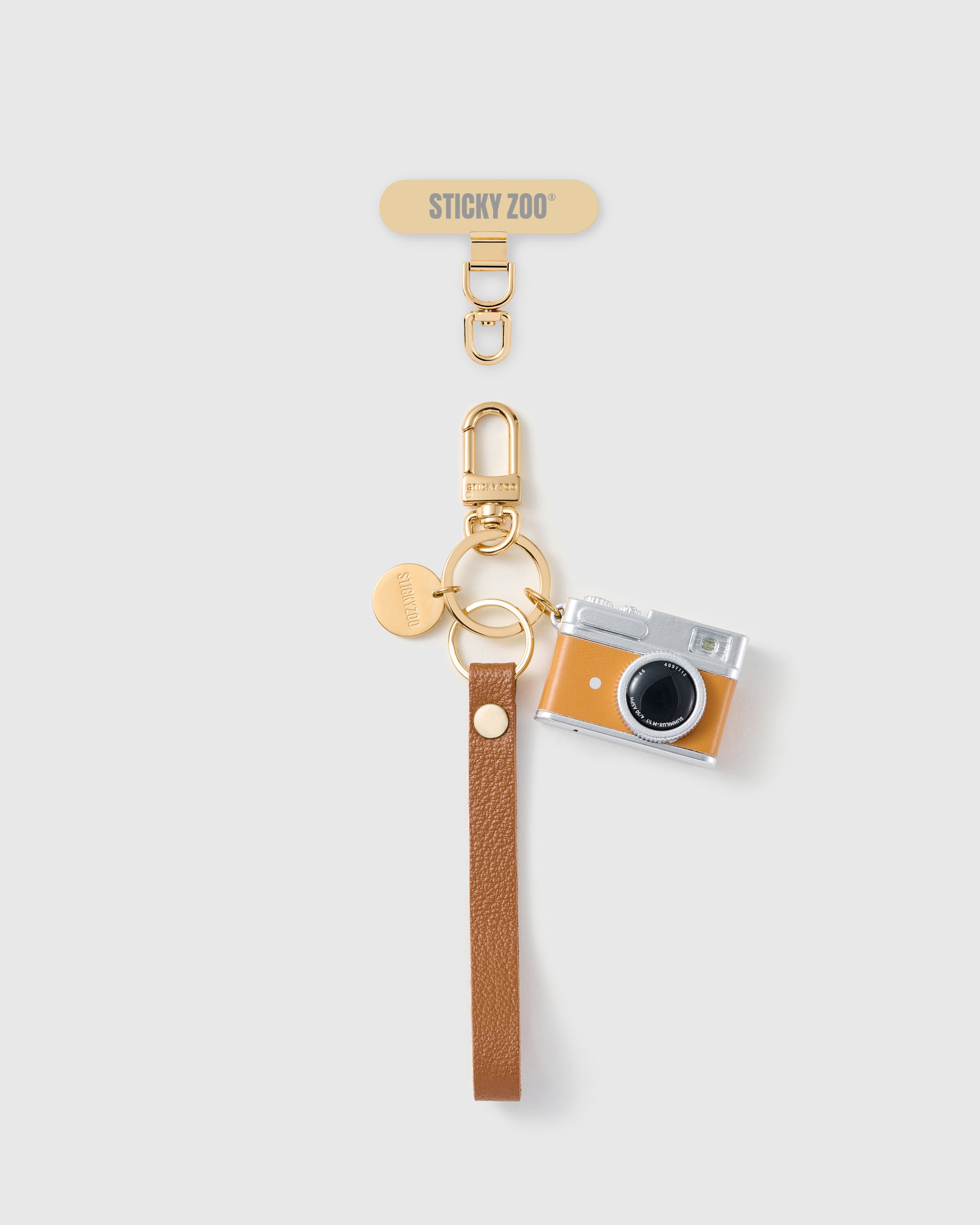 Handmade French Alran cocoa tan leather phone strap with vintage-style tangerine camera charm and 18K gold STICKYZOO hardware
